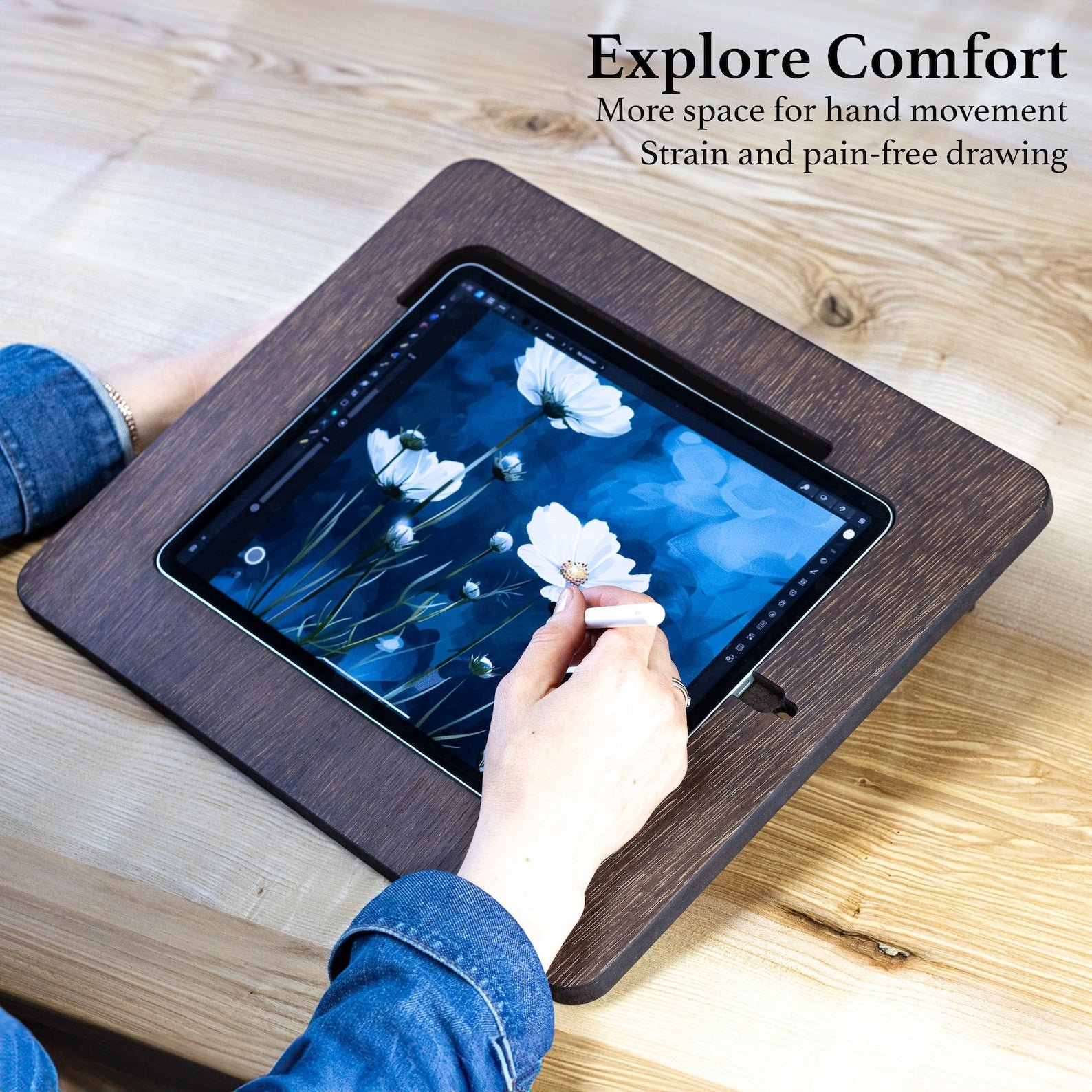 A wooden frame for an pad that is put on the table and being used by a woman, making a drawing on the device